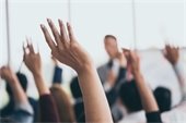 Image of students in a classroom with hands raised