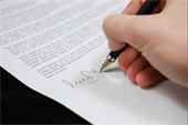 Image of a hand with pen signing a document